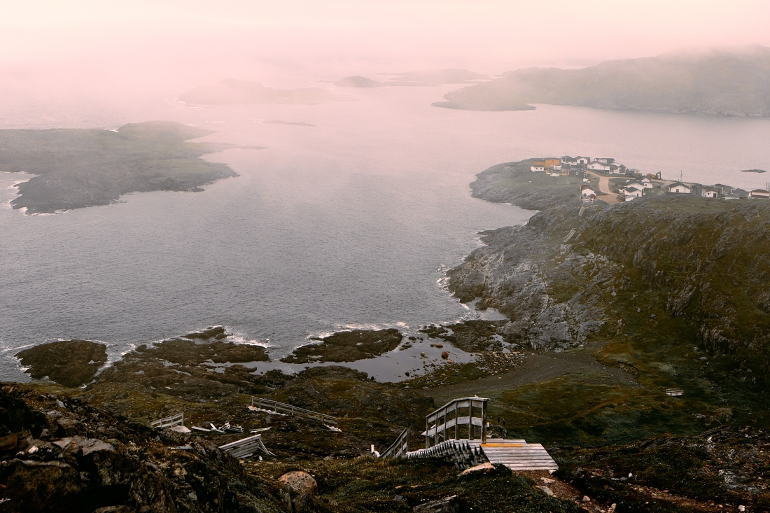 From a hilltop, mist over a harbour and scattered islands, with a wooden lookout and stairs in the foreground.